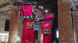Installazione con grandi tessuti fucsia sospesi tra le colonne dell’Arsenale alla Biennale Arte 2026