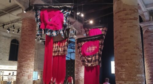Installazione con grandi tessuti fucsia sospesi tra le colonne dell’Arsenale alla Biennale Arte 2026